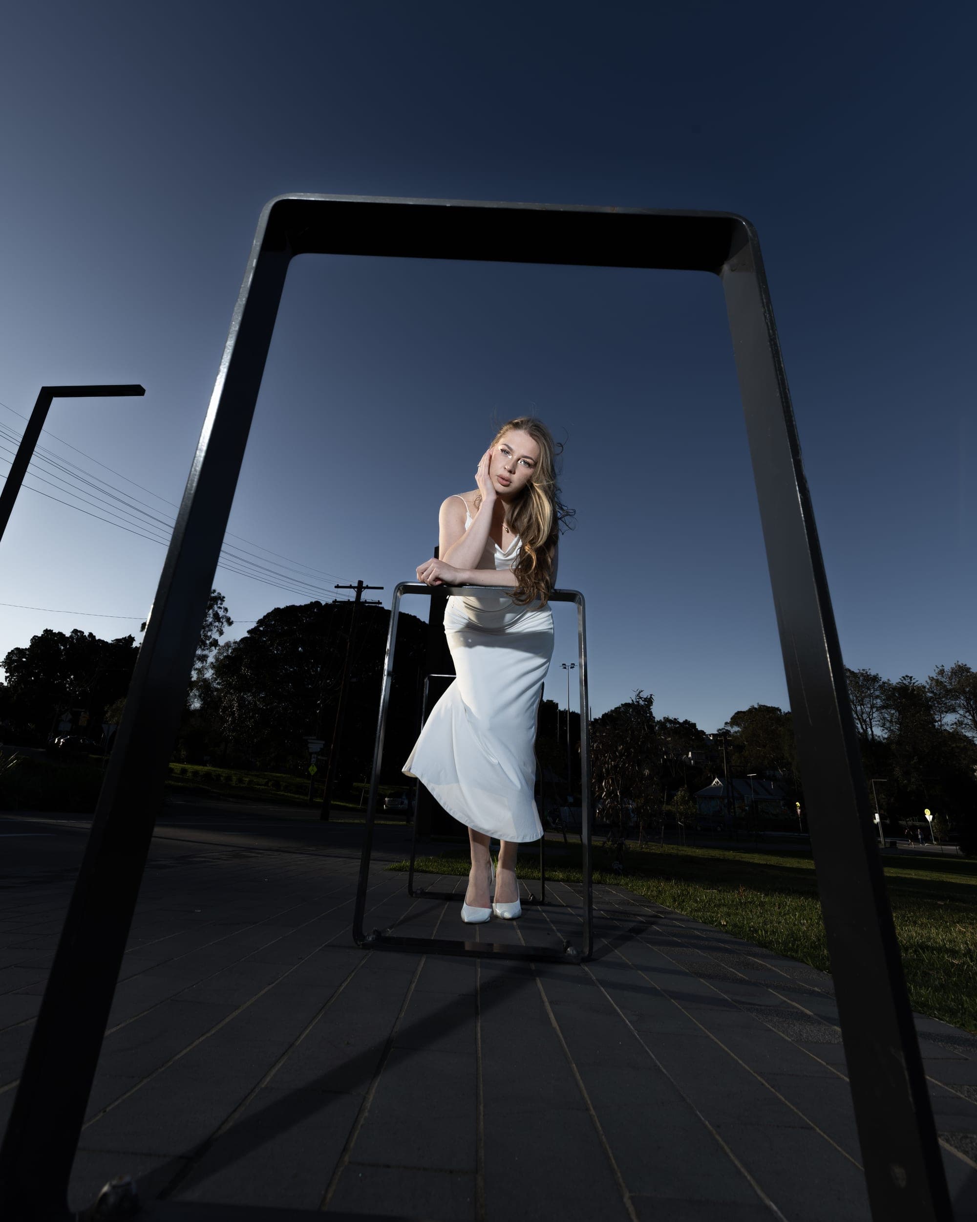 Model in a white dress leaning on a steel railing at dusk, Sydney fashion editorial