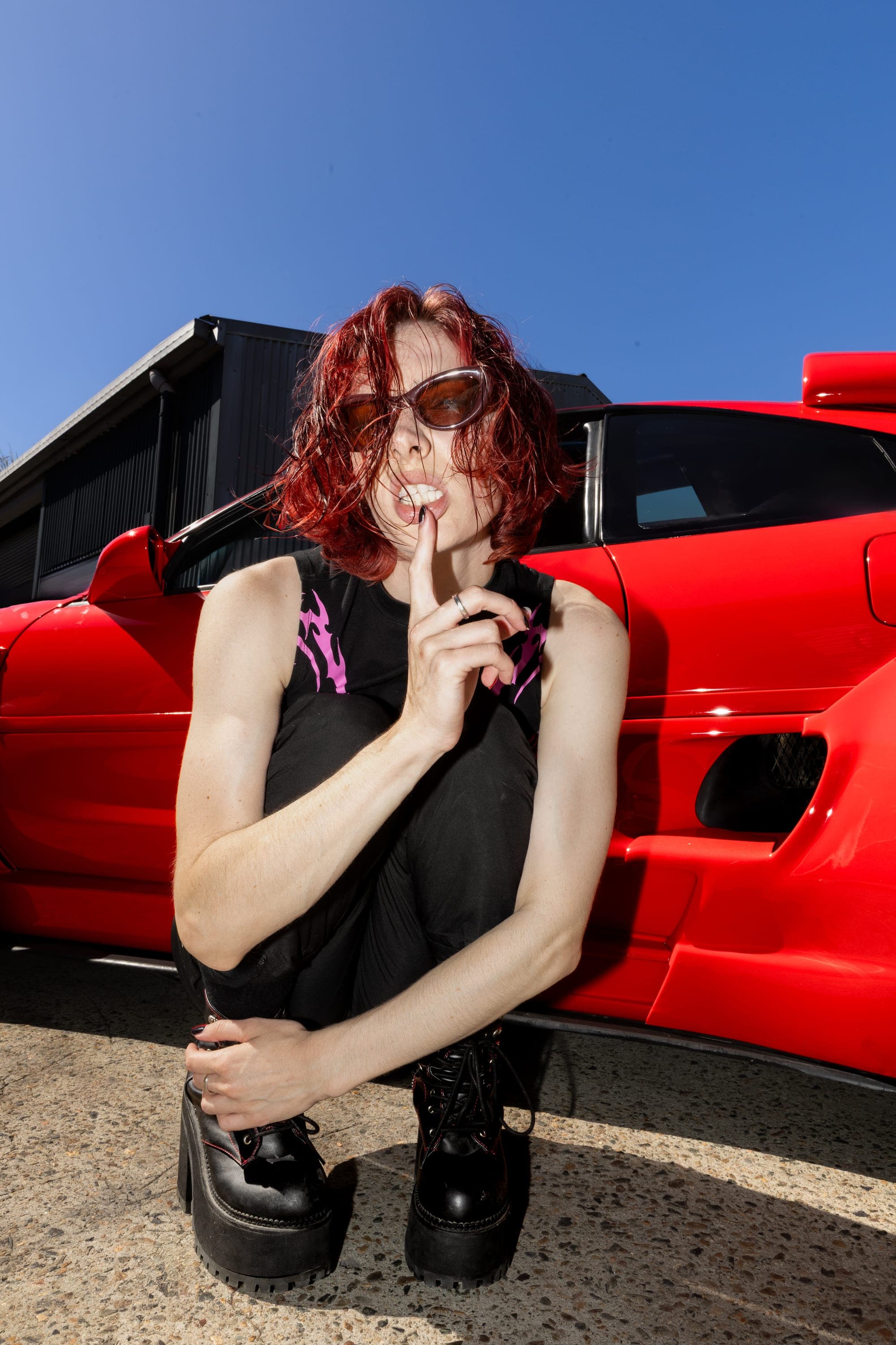 Model crouched beside a red sports car in sunglasses, edgy Sydney streetwear photography