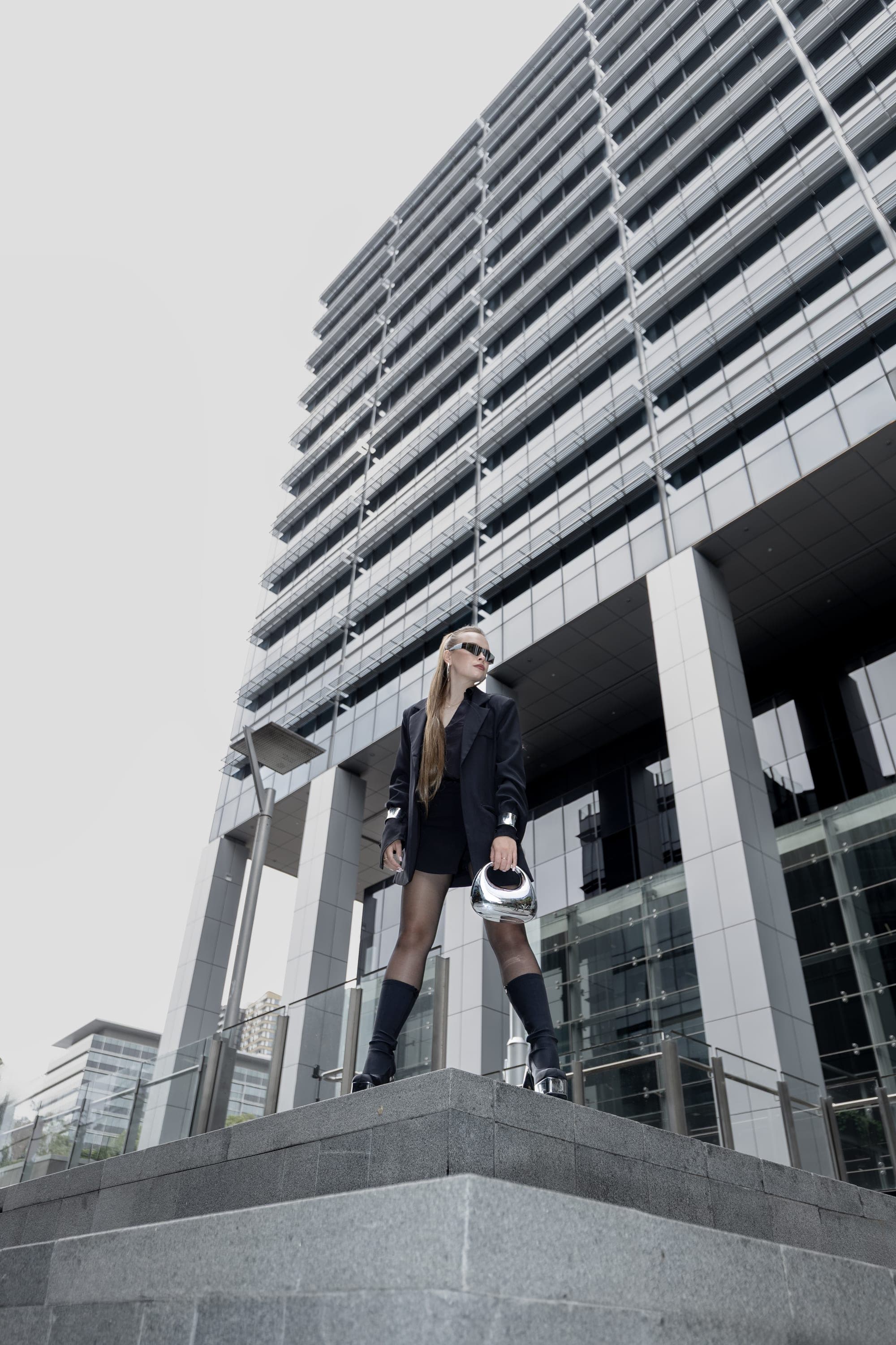 Model in a black suit standing on a ledge against a Sydney office tower, street fashion photography