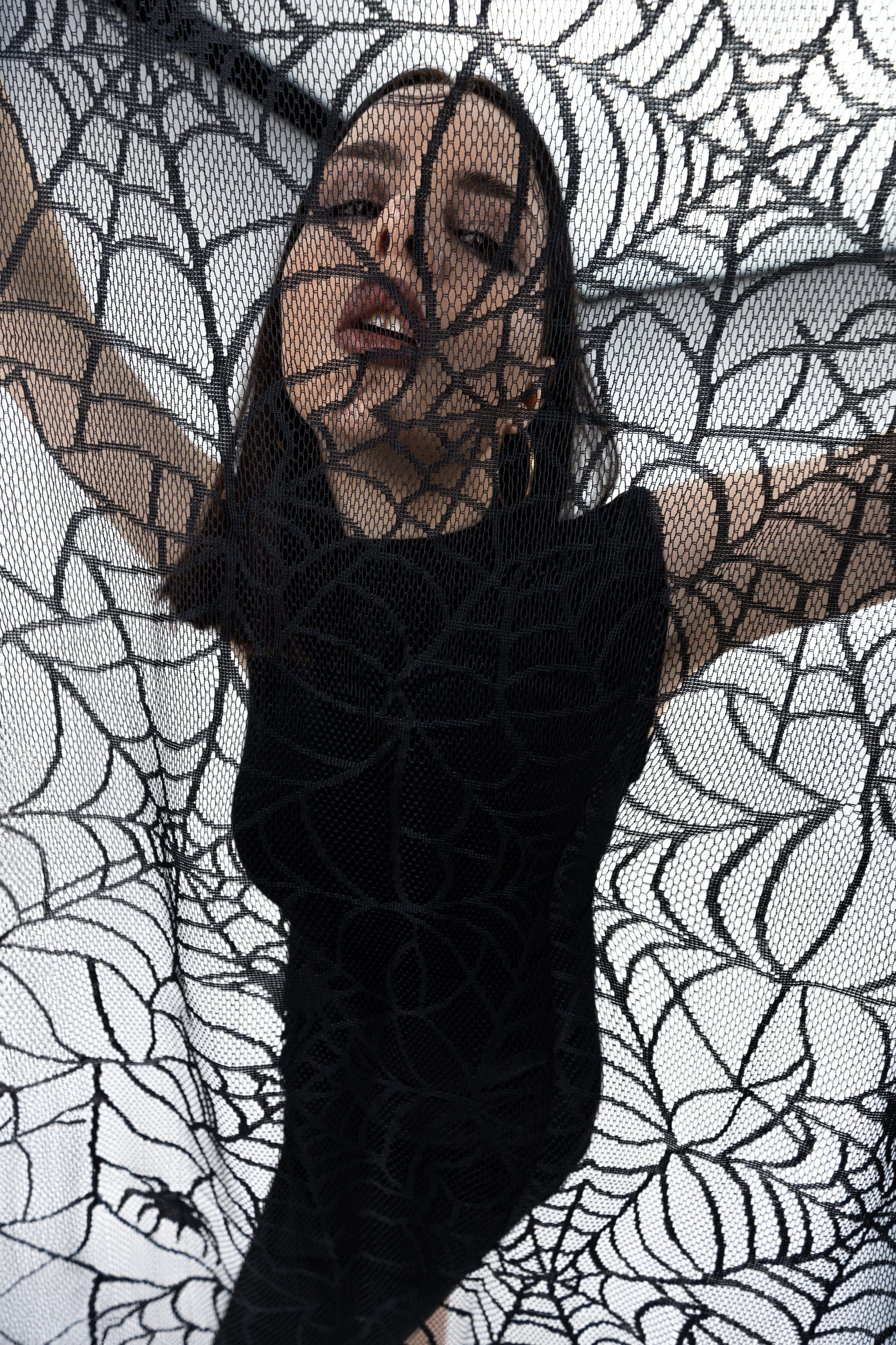 Close-up of a model behind spiderweb lace fabric, Halloween-themed studio photography